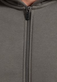 Gros plan sur un hoodie gris zippé montrant le tirette de la fermeture éclair et les détails de couture sur le tissu.