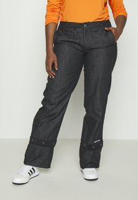 Svarta jeans med avslappnad passform, med svarta tygdetaljer vid bensluten och en knappstängning. Kombinerad med vita och svarta sneakers.