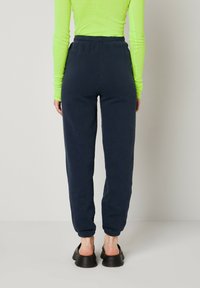Pantalons de jogging bleu marine avec taille et poignets élastiques, fabriqués en matériau doux, associés à un haut à manches longues vert vif et à des chaussures noires.