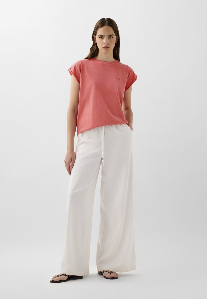 Completo composto da una maglietta corta corallo a maniche corte abbinata a pantaloni bianchi leggeri e a gamba larga. L'outfit presenta una vestibilità comoda e dettagli di cucitura discreti.