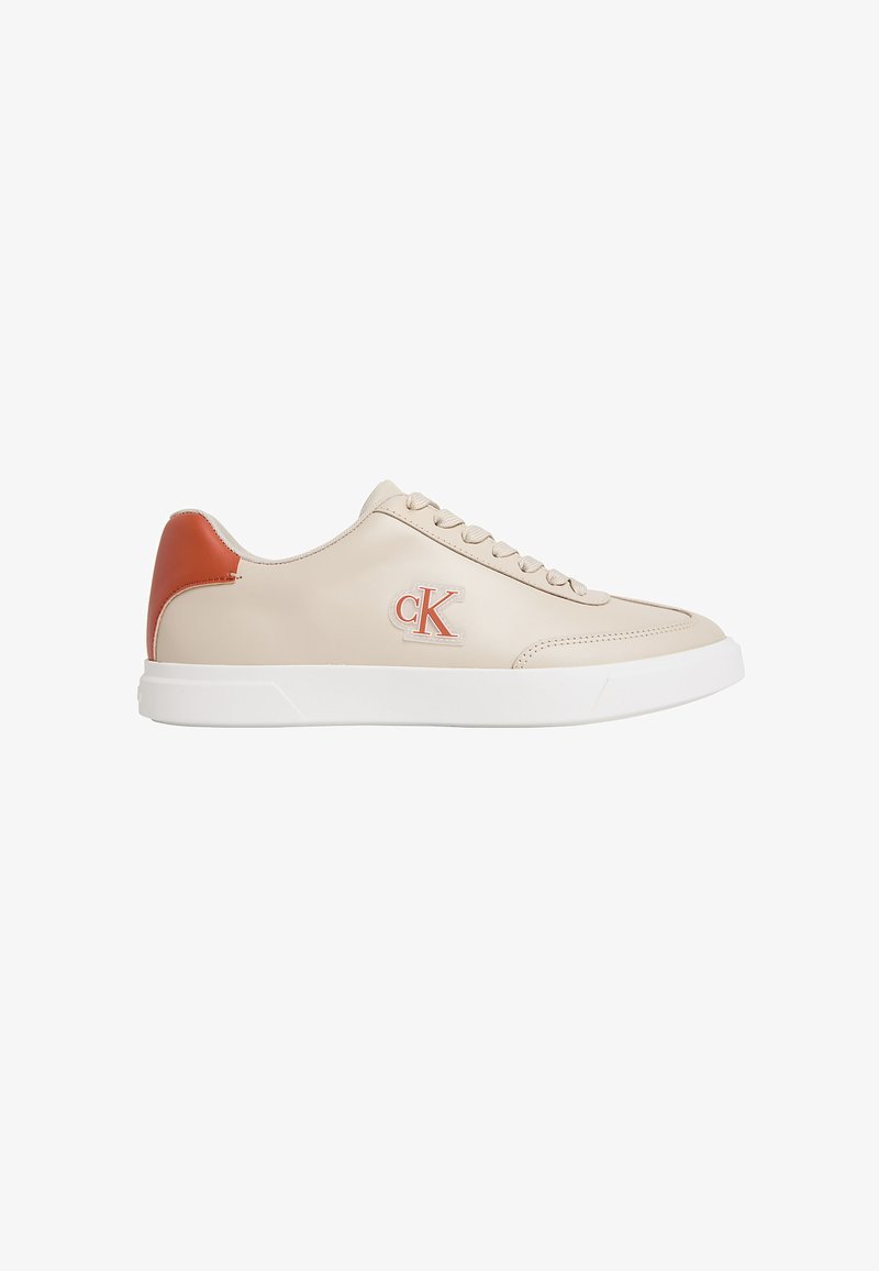 Baskets basses beige avec semelle blanche, accent orange au talon, devant à lacets, et logo "cK" orange sur le côté.