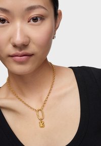 Collar de cadena de oro con un eslabón sobredimensionado y un colgante en forma de flor. La cadena tiene un acabado texturizado, mientras que el colgante es liso.