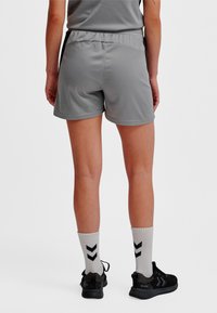 Grå sportshorts med elastisk midjeband och slät textur. Svarta detaljer längs sidorna. Svarta sneakers och randiga strumpor.