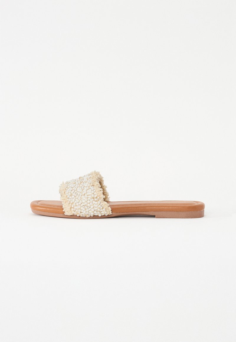 Sandale à glissière texturée en crème avec une large sangle duveteuse et une semelle lisse couleur tan. Conception plate, adaptée à un usage décontracté.