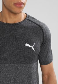 Šedé sportovní tričko s texturovaným vzorem, krátkými rukávy a bílým logem Puma na hrudi. Má kulatý výstřih a raglánové rukávy.