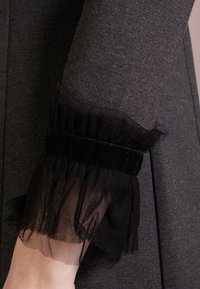 Mörkgrå ärm med en volangkant av svart tyll och ett bånd av sammet, som framhäver kontrasterande textur och design detaljer.