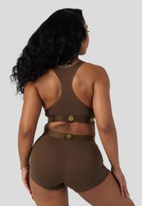 Brun atletisk bralette og matchende shorts med racerback-design. Stoffet ser glatt ut, med elastiske bånd merket med gullaksenter.