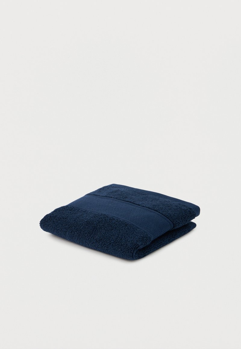 Donkerblauwe opgevouwen badhanddoek met een textuurrijke streepdetail op een effen witte achtergrond.