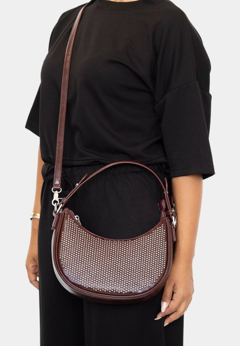 Bolso de cuero burdeos con diseño trenzado y acentos metálicos, que presenta una forma curva y una correa ajustable para llevar cruzado.