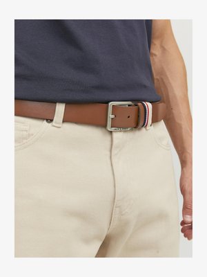 Cinturón de cuero marrón con una hebilla rectangular de plata. Presenta un acento a rayas en rojo, blanco y azul cerca de la hebilla. Lleva puesto sobre pantalones beige.
