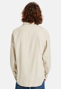 Beige long-sleeve shirt with a straight cut, back yoke seam, button cuffs, and a smooth fabric texture. Tailored and casual style.