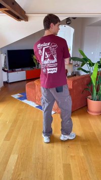 Νεαρός άνδρας φορεί μια καφέ γραφική μπλούζα Levi's και γκρι cargo παντελόνι, στέκεται σε ένα σύγχρονο σαλόνι με ξύλινο πάτωμα και μια γλάστρα με φυτό.