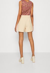 Pantaloni corti beige con una cintura elastica, abbinati a un top senza maniche con motivo floreale in rosa tenue. Tessuto morbido e vestibilità comoda.