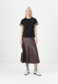 Black t-shirt with patterned cuffs, paired with a wide burgundy leather skirt. Accessories include a small white bag and grey socks.