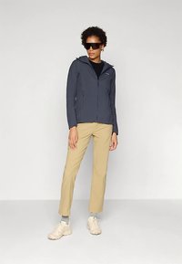 Tamsiai mėlyna lengva užtrauktuku užsegama striukė su kapišonu, derinama su smėlio spalvos kelnėmis. Modelis dėvi saulės akinius ir šviesios spalvos batus su pilkomis kojinėmis.