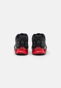 Pair of black athletic shoes with red heels, mesh upper, and reflective details, shown from the back on a white surface.