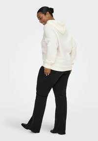 Lys kremhvit hettegenser med stor hette, ribbestrikkede mansjetter og nederkant, kombinert med svarte vide jeans og svarte sko. Enkel, avslappet antrekk.