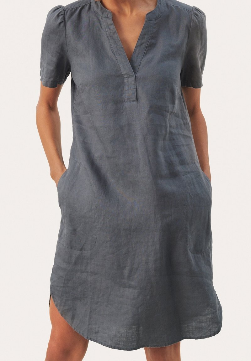Robe manches courtes atteignant le genou, en tissu doux et texturé gris foncé. Caractérisée par un col en V et des poches latérales. Ourlet légèrement arrondi.