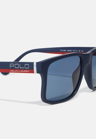 Occhiali da sole blu navy con lenti grigie. La montatura opaca presenta accenti a strisce rosse e bianche con il marchio "POLO" e "RALPH LAUREN" sul lato.