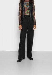 Black leather vest over a colorful patterned long-sleeve top, paired with wide-leg black jeans and black ankle boots.