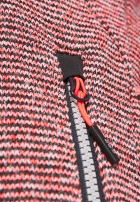 Tissu tricoté avec un motif à rayures rouges et noires ; comporte une fermeture éclair noire avec un tirette orange pour la fixation.