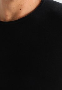 Zwarte T-shirt met een ronde halslijn, gemaakt van ribkatoen. Textuurstof met een strak aansluitend ontwerp, dat detail van de hals en bovenborst laat zien.