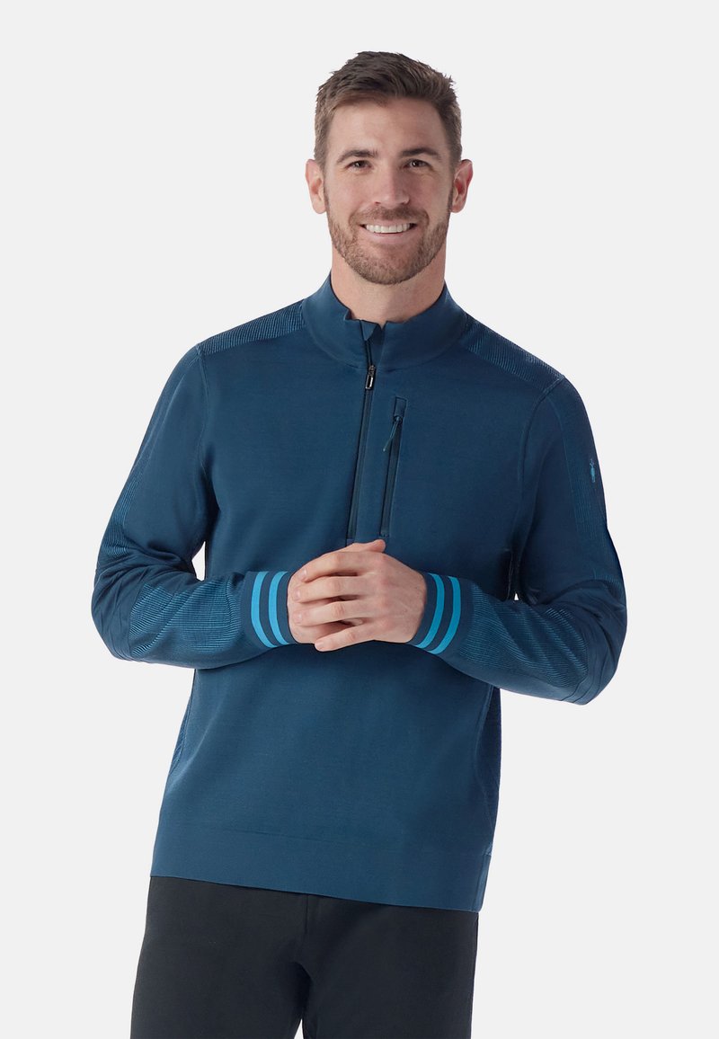 Maglione da uomo con zip di un profondo teal, dotato di un colletto rialzato, dettagli texturizzati sulle spalle e polsini a righe teal. Tessuto liscio, design aderente.