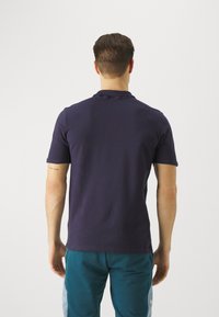 Marineblaues kurzärmliges Polohemd aus strukturiertem Stoff, mit einem einfachen Kragen und geradem Saum. Es wird mit türkisen Hosen getragen.
