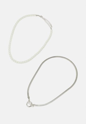 Två halsband: det ena är en rad vita pärlor med en metalldel, det andra är en tunn silverkedja med en cirkulär lås.