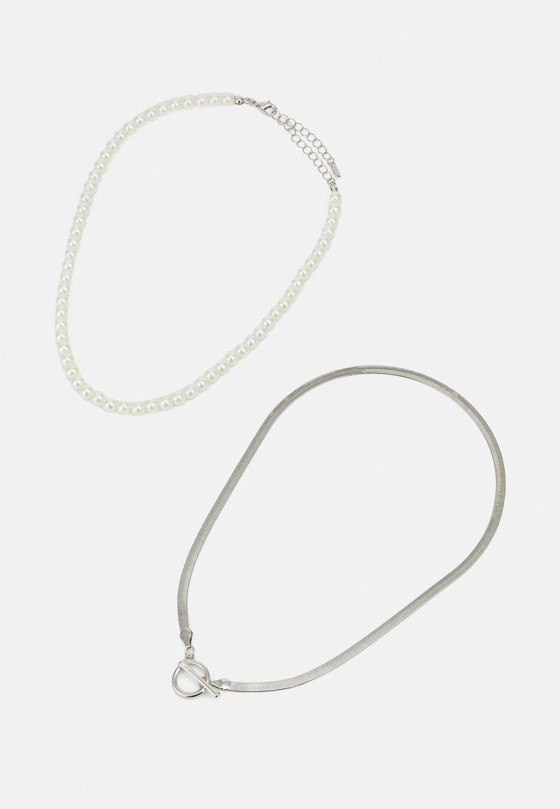 Dwa naszyjniki: jeden to sznurek białych pereł z metalowym zapięciem, drugi to cienki srebrny łańcuszek z okrągłym zapięciem.