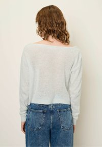 Pull en tricot lâche bleu clair avec un décolleté large, des manches longues et un ourlet court, associé à un jeans taille haute délavé.