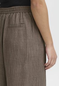 Braune Stoffhosen mit strukturiertem Finish, ausgestattet mit vertikalen, dünnen weißen Streifen, einem elastischen Bund und einer dezenten Gesäßtasche.