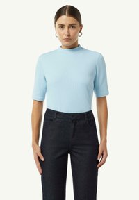 Jasnoniebieska prążkowana bluzka z krótkim rękawem i wysokim dekoltem, w połączeniu z ciemnoniebieskimi spodniami z wysokim stanem.
