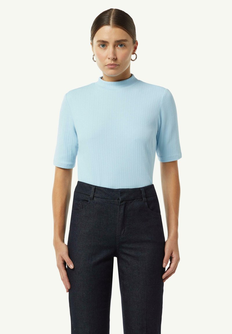 Jasnoniebieska prążkowana bluzka z krótkim rękawem i wysokim dekoltem, w połączeniu z ciemnoniebieskimi spodniami z wysokim stanem.