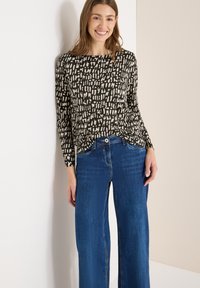 Czarny top z długim rękawem ozdobiony abstrakcyjnymi beżowymi wzorami, zestawiony z niebieskimi, szerokimi spodniami dżinsowymi. Materiał wydaje się miękki, a krój luźny.