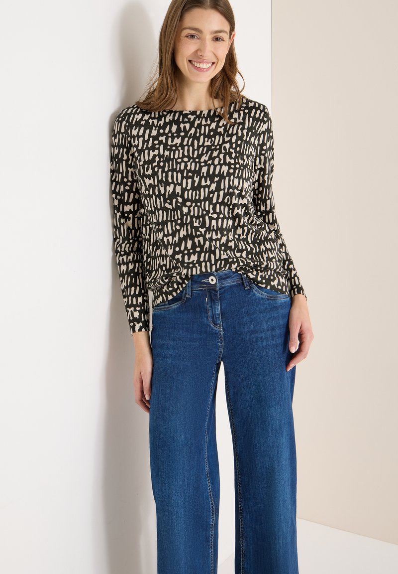 Czarny top z długim rękawem ozdobiony abstrakcyjnymi beżowymi wzorami, zestawiony z niebieskimi, szerokimi spodniami dżinsowymi. Materiał wydaje się miękki, a krój luźny.