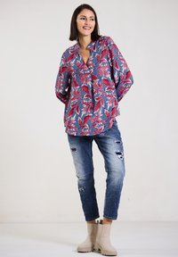 Floral long-sleeve blouse in blue, red, and green, paired with distressed light blue jeans and beige ankle boots. Effortless fit and design.