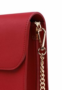 Červená kožená taška s hladkým povrchem, vybavená řetízkovým popruhem a zapínáním ve zlatém tónu. Design s překlopným klopovým uzávěrem a čistými švy.