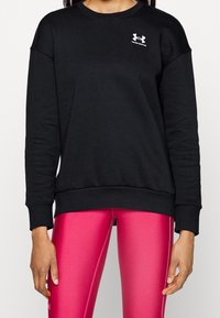 Black sweatshirt with long sleeves, crew neck, and ribbed hem. Features a small white logo on the chest. Paired with bright pink leggings.