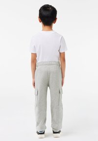 Pantalon de survêtement gris avec poches cargo, taille élastique et poignets, associé à un t-shirt blanc uni, vu de dos.
