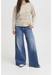 Chemise à manches longues rayée beige et crème associée à un jean en denim bleu à jambes larges ; texture lisse avec un dégradé progressif à l'ourlet.