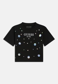 Μαύρο κοντομάνικο μπλουζάκι με αντανακλαστικές στρογγυλές λεπτομέρειες και λευκό κείμενο "GUESS EST.1981", κατασκευασμένο από βαμβακερό υλικό.