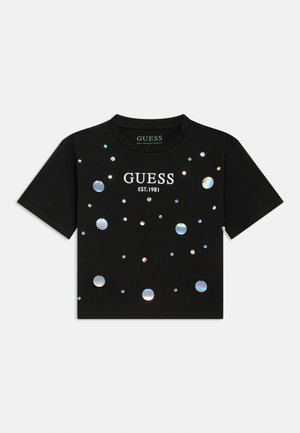 Fekete rövid ujjú póló, visszaverő kerek díszítésekkel és fehér "GUESS EST.1981" felirattal, pamut anyagból készült.