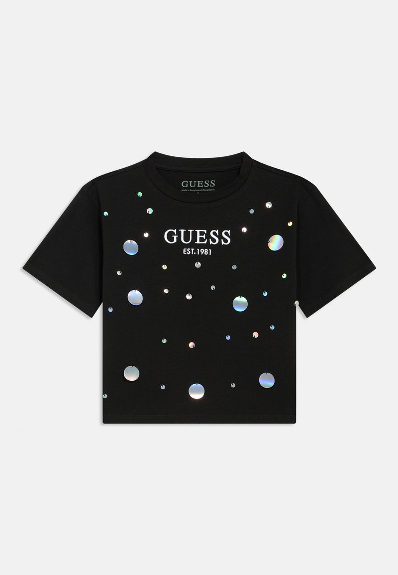 Μαύρο κοντομάνικο μπλουζάκι με αντανακλαστικές στρογγυλές λεπτομέρειες και λευκό κείμενο "GUESS EST.1981", κατασκευασμένο από βαμβακερό υλικό.