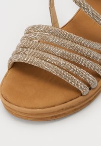Sandalo con cinturini, dotato di una soletta in suede marrone chiaro, arricchito da multiple bande scintillanti in metallo argentato sulla parte superiore.
