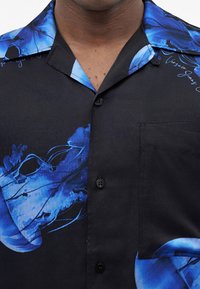 Μαύρο πουκάμισο με κουμπιά με μπλε μοτίβο μέδουσας και τσέπη στο στήθος, φορεμένο από άτομο με σκουρόχρωμο δέρμα.