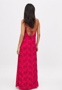 Robe longue rose avec un motif floral noir, bretelles spaghetti et un dos ouvert maintenu par un lien. Tissu doux avec une silhouette fluide.