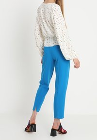 Blusa in cotone con pois multicolori, abbinata a pantaloni blu su misura con orlo spaccato. Sandali con tacco largo e dettagli colorati.