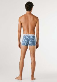 Blaue bedruckte Boxer-Shorts aus Baumwolle mit einem weißen Bund, auf dem der Markenname steht. Das Design umfasst kleine, wiederholte Motive.