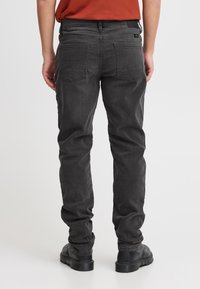 Tumedat halli teksapüksid sirge säärega, millel on tagataskud ja sile pind, kantud mustade saapade ja roostevärvi särgiga.